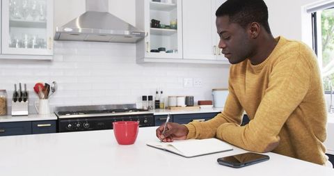 Man writing at modern kitchen counter with coffee mug