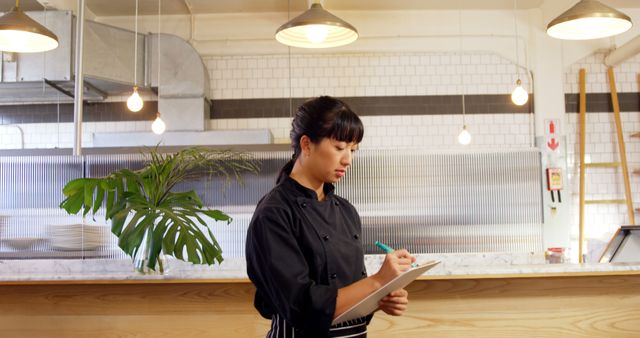 Asian Female Chef Taking Notes in Modern Restaurant Kitchen - Download Free Stock Images Pikwizard.com