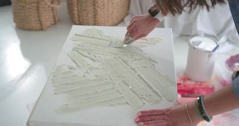 Artist spreading modeling paste on stretched canvas with palette knife in bright studio