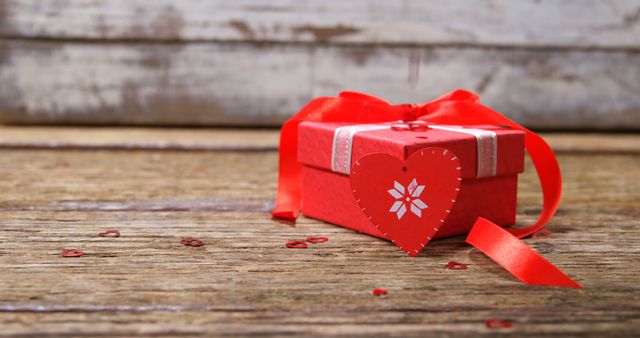 Small red gift box with heart-shaped decoration and a ribbon on a rustic wooden surface. Suitable for holiday, romantic, Valentine's Day, anniversary, and special occasion themes.