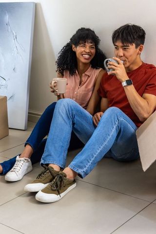 African american woman and asian man unpacking, enjoying coffee and smiling in new home