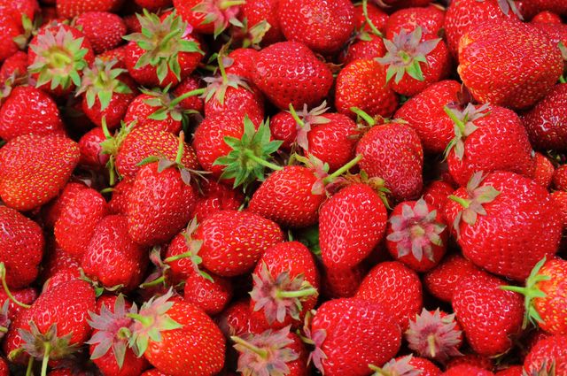 Vibrant close-up view of numerous fresh strawberries, showcasing their vivid red color and green leaves. Ideal for use in food blogs, healthy eating promotions, recipe illustrations, and advertisements for organic produce.