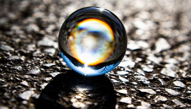 Crystal sphere on textured pavement with prismatic rainbow reflection and deep shadow