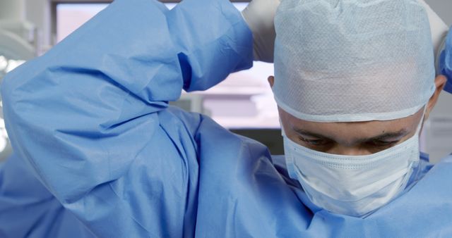 Close-up of a surgeon preparing for an operation in a surgical room, putting on a mask and adjusting head cover. Useful for illustrating medical preparation, healthcare professions, hospital scenes, and the importance of sterile environments in surgeries.