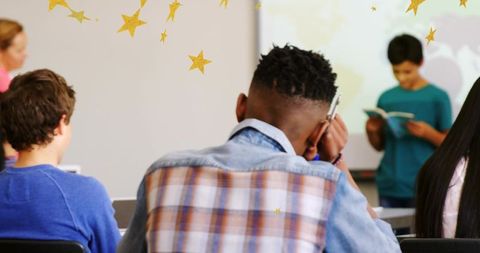 Student taking notes while classmate reading aloud in modern classroom learning
