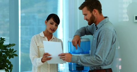 Young professionals discussing document at workplace water cooler