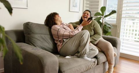 African American Friends Laughing on Couch Sharing Smartphone in Cozy Living Room