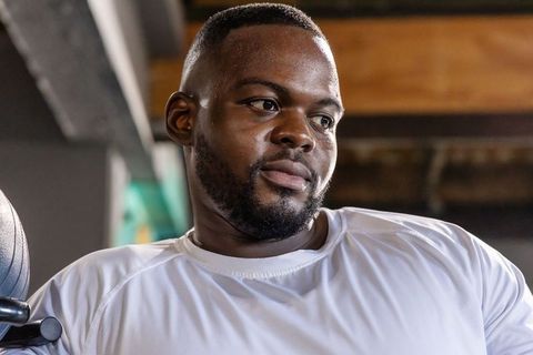 Gym athlete leaning on machine gripping knob, focused expression, perspiring after workout