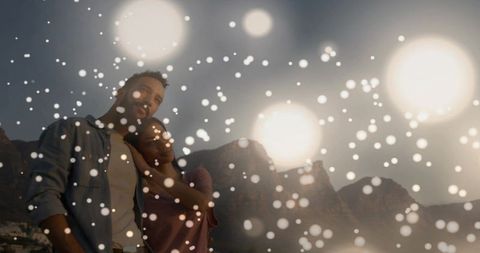 Romantic couple embracing on coastal hillside at sunset with dreamy bokeh lights