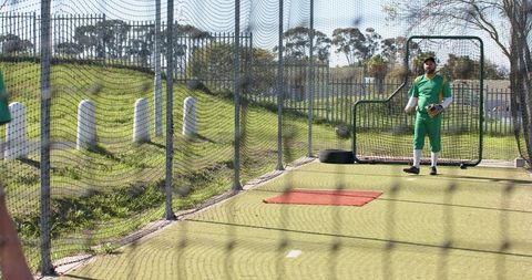 Mid-adult baseball teammates practicing in batting cage wearing green uniforms and gloves