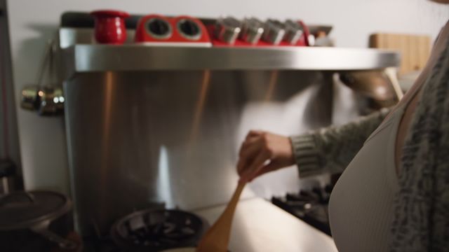 This image captures a side view of a woman with long blonde hair frying eggs with a spatula on a stove. Perfect for use in cooking blogs, kitchen appliance promotions, or menus for breakfast recipes. Highlights the warmth and intimacy of home cooking in a cozy kitchen environment.