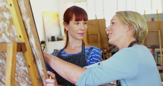 This image portrays an art teacher advising a student during a painting class. Use it for representing educational settings, art workshops, creative learning environments, or showcasing mentorship and guidance in artistic skills.