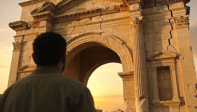 Traveler standing before ancient cracked roman arch at sunset