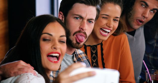 Friends making funny faces and taking a selfie on mobile phone in restaurant