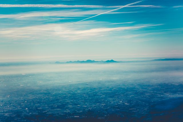 Ideal for travel agencies promoting scenic destinations, websites about nature and landscapes, backgrounds for presentations, or wallpapers. This image captures the beauty of nature from above, showcasing fog-covered mountains with a clear blue sky and clouds above a vast landscape.