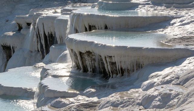 Sunlit travertine terraces cascading with turquoise thermal pools and mineral drips