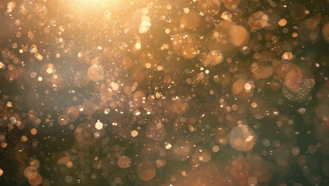 Golden bokeh particles floating in warm backlit glow, glittering abstract background