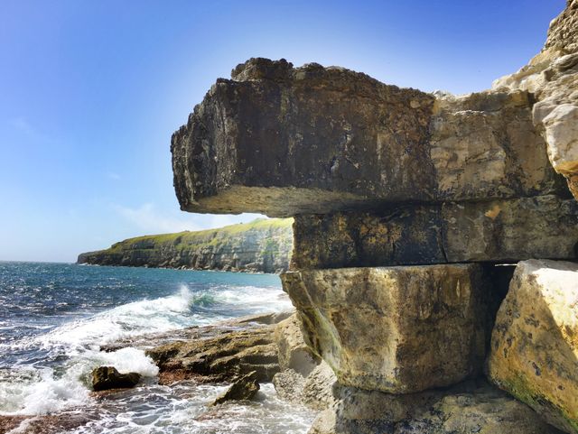 Dramatic rock formation on coastal cliff overlooking the ocean with waves crashing against the rocky shore. Ideal for use in travel-related content, nature documentaries, environmental studies, and tourism promotions. Emphasizes natural beauty, power of erosion, and scenic vistas.