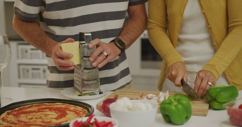 Couple preparing homemade pizza with fresh ingredients in modern kitchen