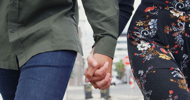 A young Caucasian couple is holding hands while walking, with copy space. Their affectionate gesture adds a romantic touch to the urban setting they're in.