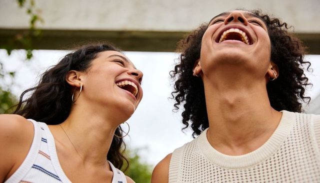 Laughing friends tilting heads back enjoying outdoor summer moment with hoop earrings