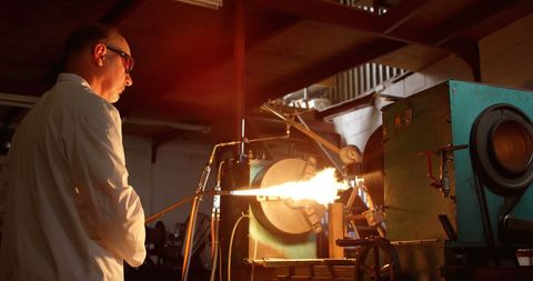 Skilled worker heating glass in industrial glass factory