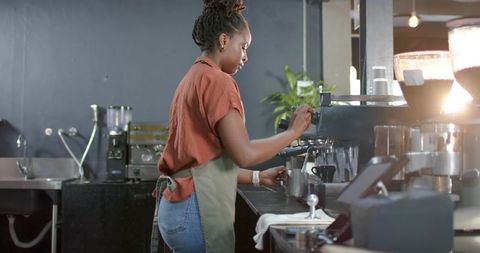 African barista preparing espresso and frothing milk behind modern cafe counter