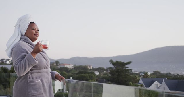 Woman in bathrobe with towel on head enjoying morning drink on balcony - Download Free Stock Images Pikwizard.com