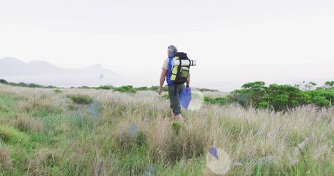 Senior hiker walking coastal grassland with backpack and sleeping pad, outdoor adventure