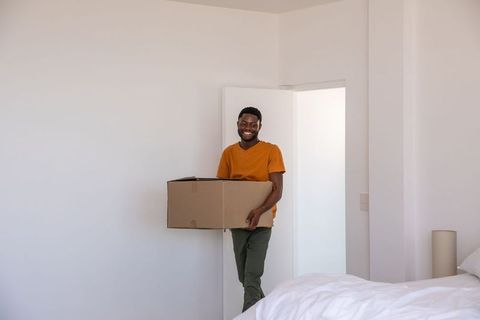 Man carries cardboard box into minimalist bedroom design