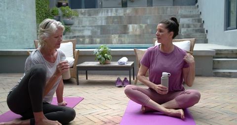 Mixed-age women practicing yoga and chatting on patio with water bottles, wellness