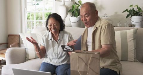Joyful asian senior couple enjoying new purchases at home
