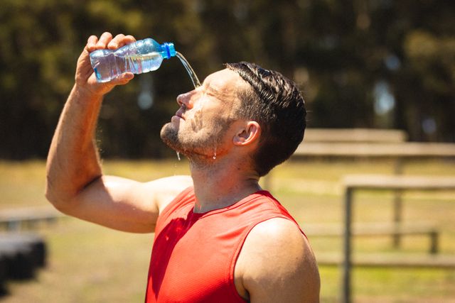 Tired caucasian mid adult man pouring water on face while standing in bootcamp ground. unaltered, fitness, athleticism, sunny, cross training and sports training.