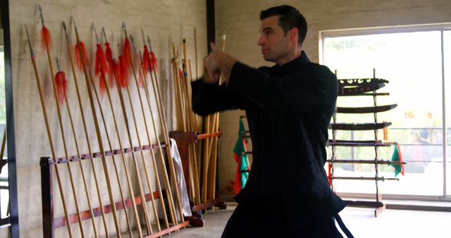 Caucasian man practices archery indoors, with copy space. Focus and precision are evident as he aims at the target in a well-lit training hall.