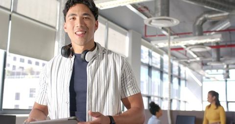 Smiling professional holding tablet wearing headphones in bright modern open-plan office