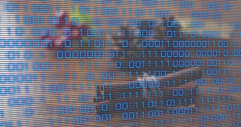 Blue binary overlay obscuring coworking desk and laptop representing cybersecurity data teamwork