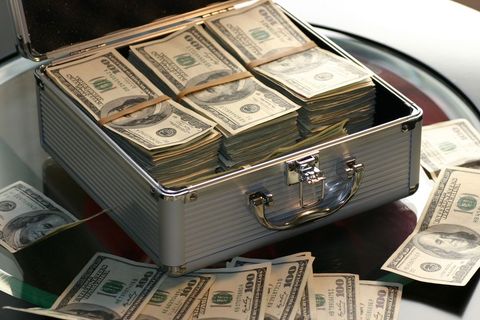 Stacks of cash in metal briefcase with scattered bills on glass table
