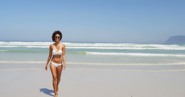 Strong beach vibe with a woman in a white bikini walking towards the camera. Ideal for summer vacation adverts, beachwear promotions, holiday brochures, and travel blogs. Showcases fun, relaxation, and enjoyment in a coastal setting.