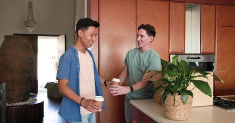Happy Male Couple Enjoying Coffee While Unpacking in New Home