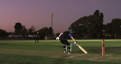 Cricket batsman driving forward shot under twilight floodlights on evening match pitch