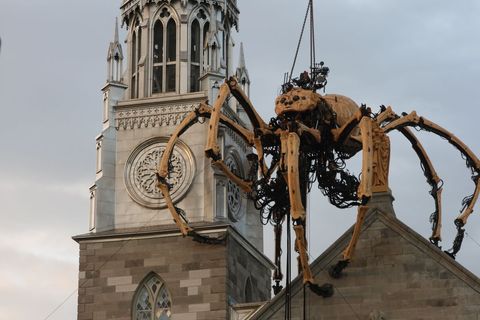 Giant mechanical spider looming over historic church tower at dusk, urban spectacle