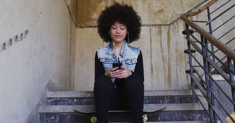 Young woman listening to music on staircase with skateboard