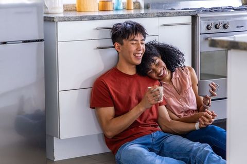 Multiracial couple sharing coffee and laughing on modern kitchen floor