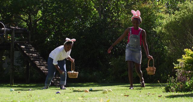African american brother and sister wearing easter bunny ears doing easter egg hunt in garden. family spending easter time together staying at home in isolation during quarantine lockdown.