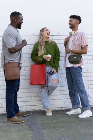 Diverse friends laughing and leaning against white brick wall holding red shopping bag