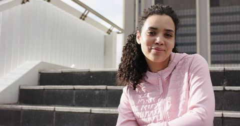 African American woman sitting on city steps wearing pastel pink jacket smiling urban portrait