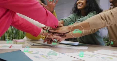 Team joining hands over sustainability charts for collaborative green strategy