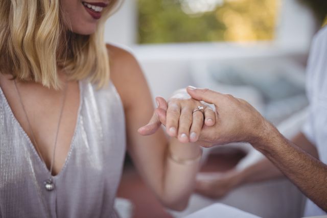 Man placing engagement ring on woman's hand in a romantic restaurant setting. Ideal for use in articles or advertisements about proposals, engagements, romantic dinners, and relationship milestones.
