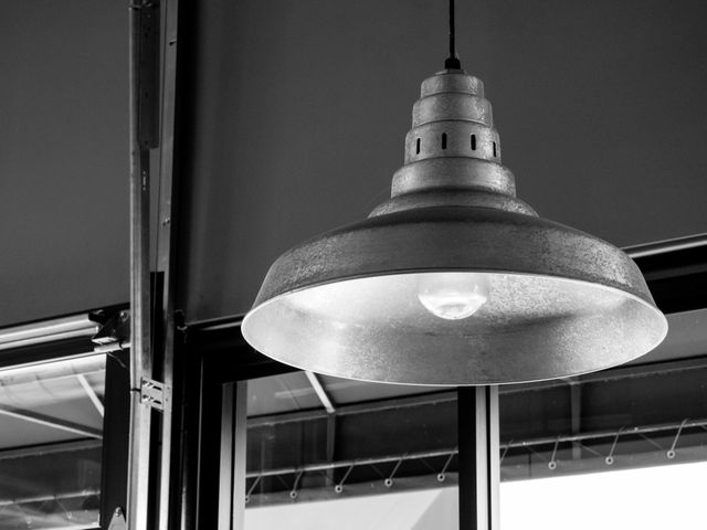 Vintage industrial pendant light hanging inside warehouse space. Black and white photograph emphasizes the texture and form of the lamp. Suitable for use in articles or blogs about interior design, industrial style decor, or minimalist living. Potential use as inspirational image for home renovation and retrofitting projects.