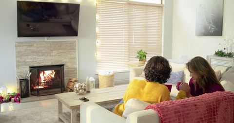 Couple Sharing Warm Drinks on Sofa by Fireplace, Cozy Living Room with Holiday Lights